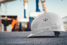 a white hard hat on the ground with a job site faded in the back