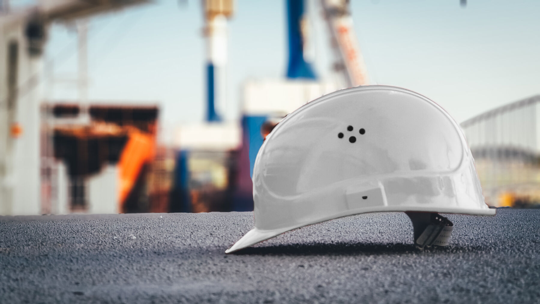 a white hard hat on the ground with a job site faded in the back